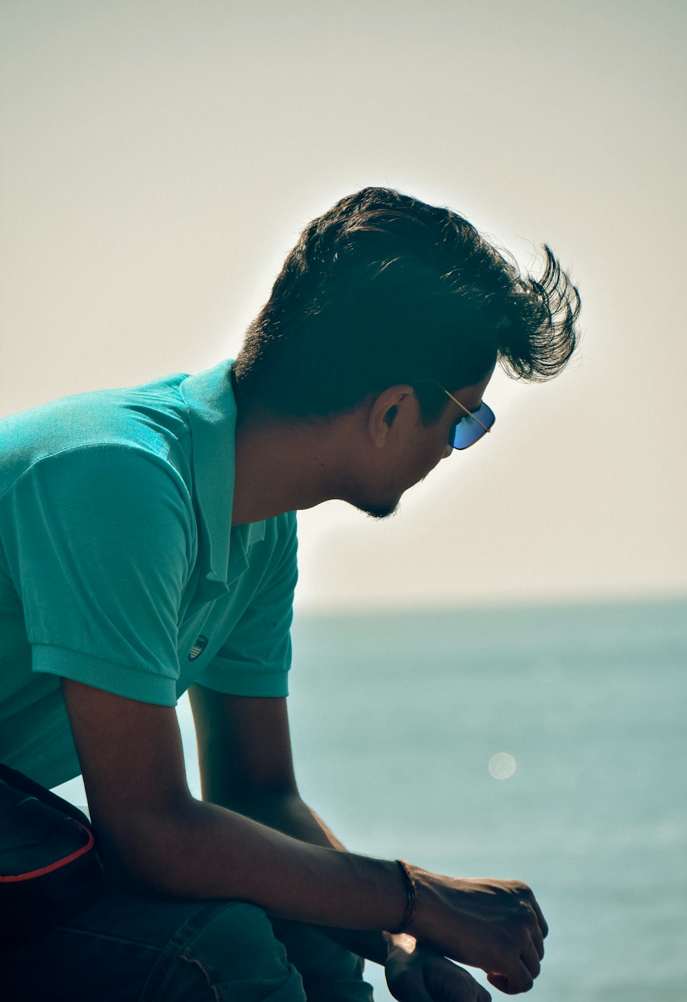 a young man sitting on a bench next to the ocean