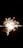 Bright sparkler emitting radiant sparks against a dark background, creating a starburst effect.