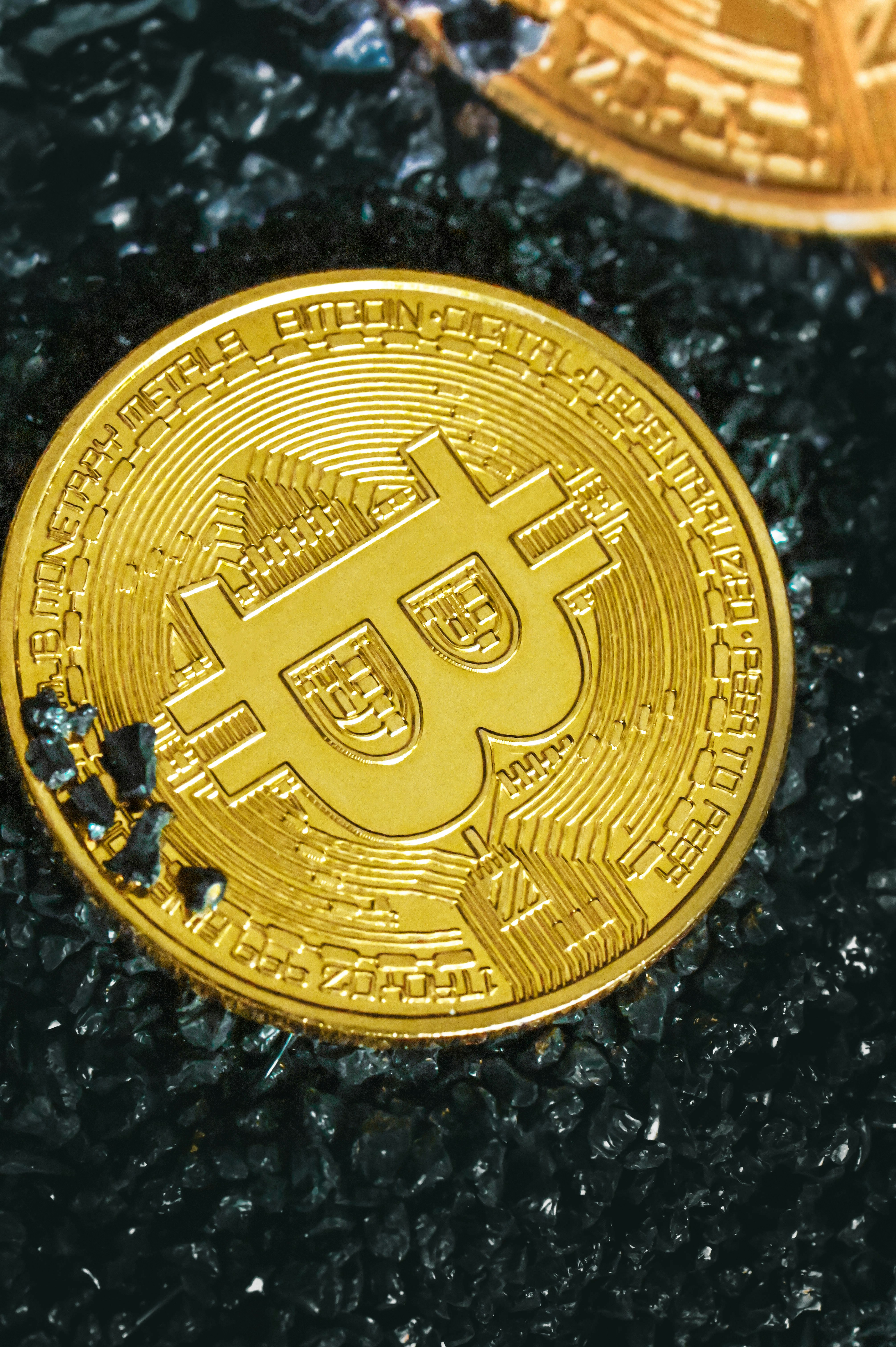 A gold Bitcoin laying on black stones