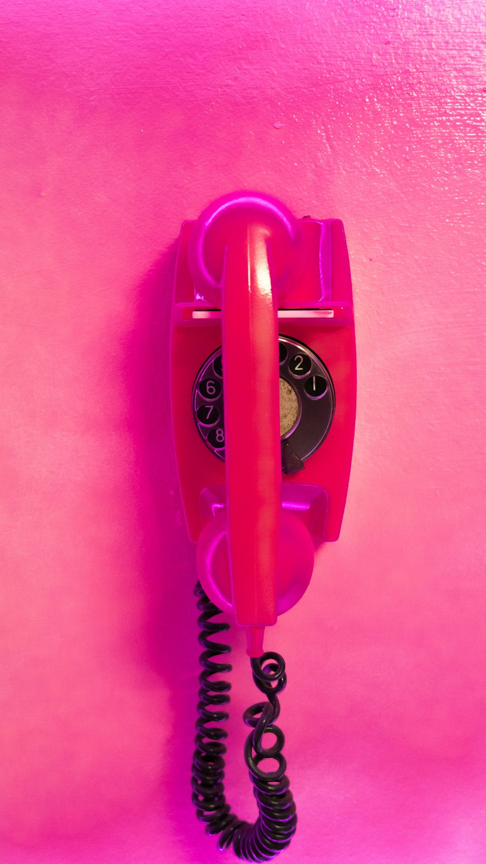 a red phone hanging on a pink wall