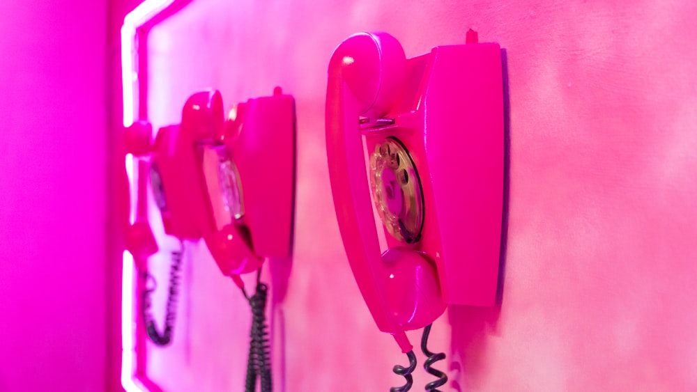 Dos teléfonos rosas están en una pared rosa