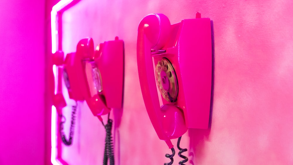 two pink telephones are on a pink wall