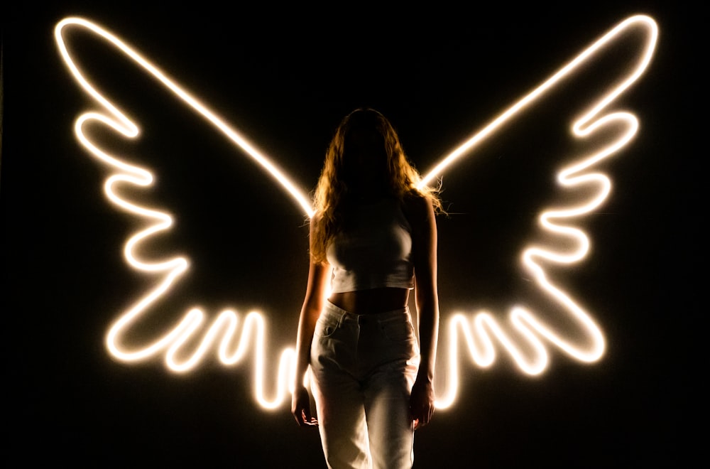 a woman standing in front of a light painting angel