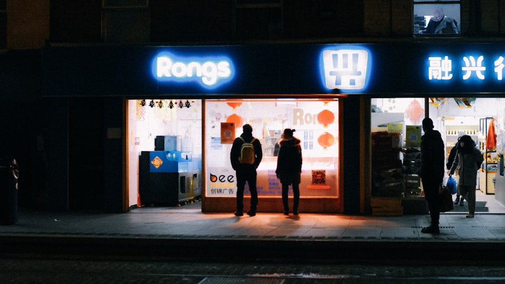 a group of people standing outside of a store at night