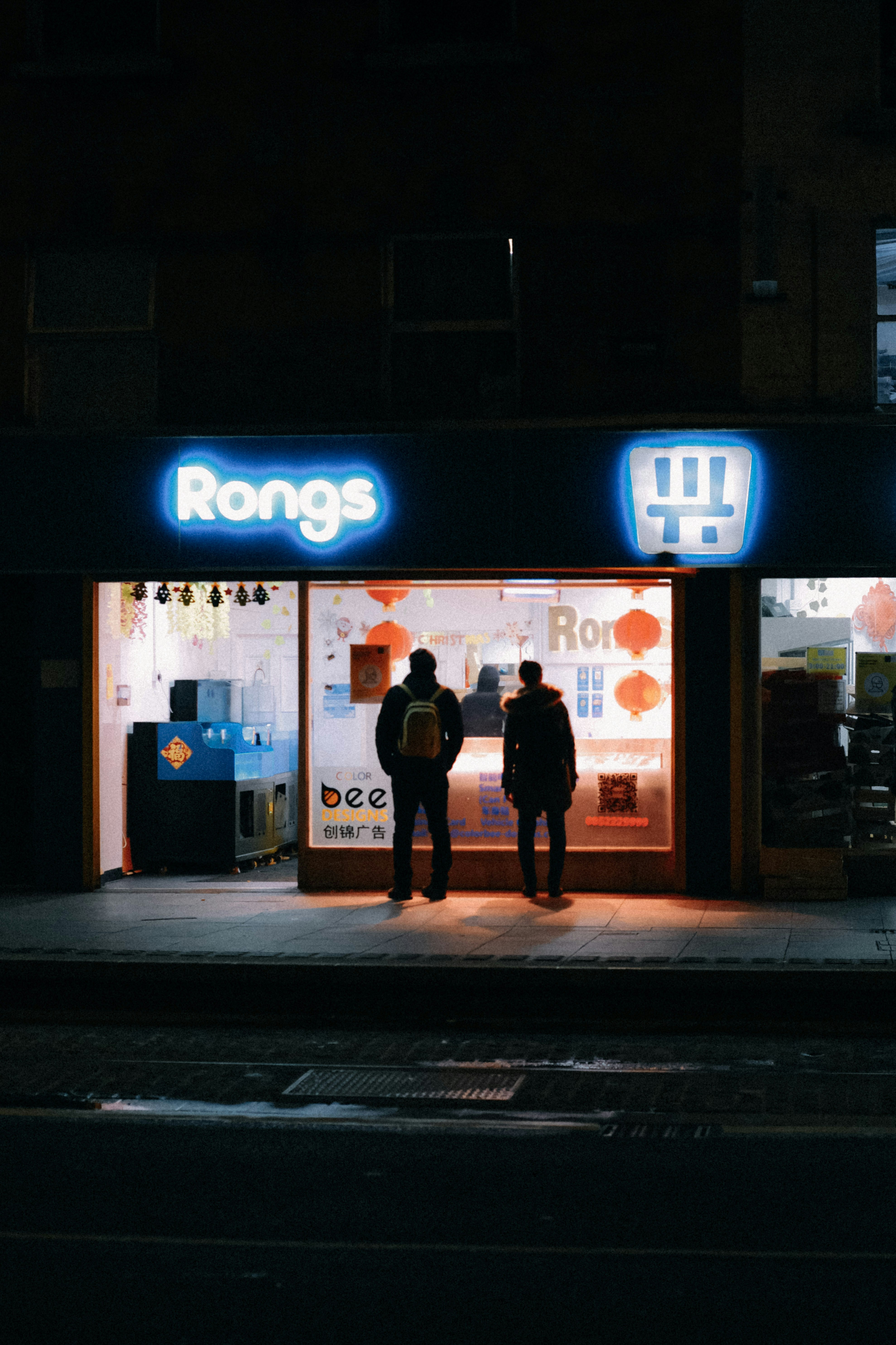 two people standing outside of a store at night