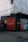 A construction site with scaffolding covered in white sheeting. The corner of the site features a black wall with repeated red text 'PAST PRESENT' and a singular 'FUTURE'. Various informational and advertisement boards are visible, promoting Clerys Quarter with images and text about work and catching up.