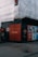 A construction site with scaffolding covered in white sheeting. The corner of the site features a black wall with repeated red text 'PAST PRESENT' and a singular 'FUTURE'. Various informational and advertisement boards are visible, promoting Clerys Quarter with images and text about work and catching up.