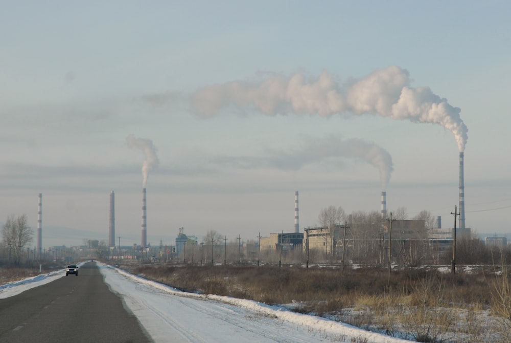 a car driving down a road with smoke stacks in the background