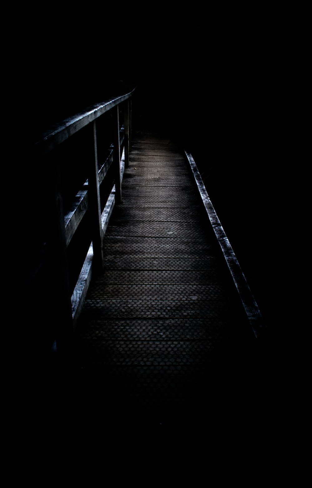 a dark walkway leading to a bench in the dark