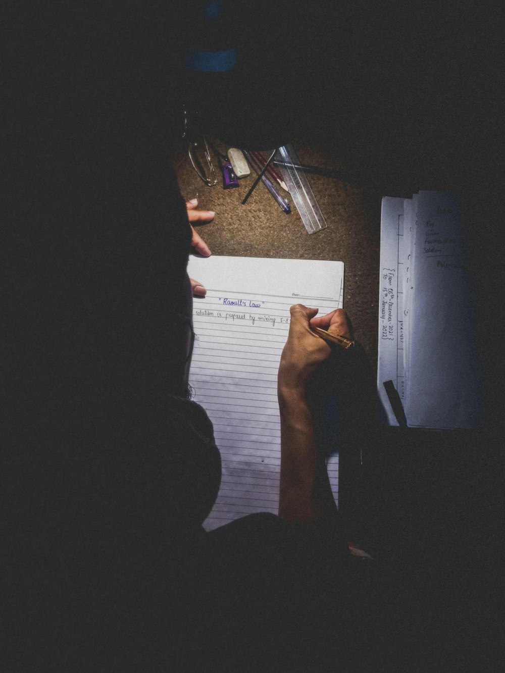 Una persona sentada en un escritorio escribiendo en un pedazo de papel