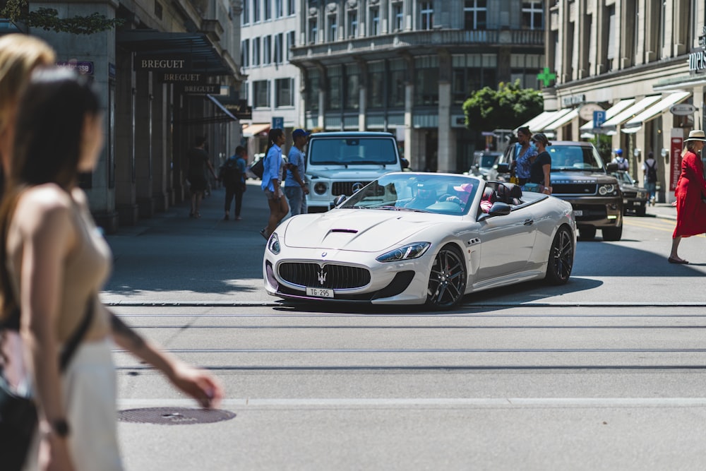 a white sports car driving down a city street