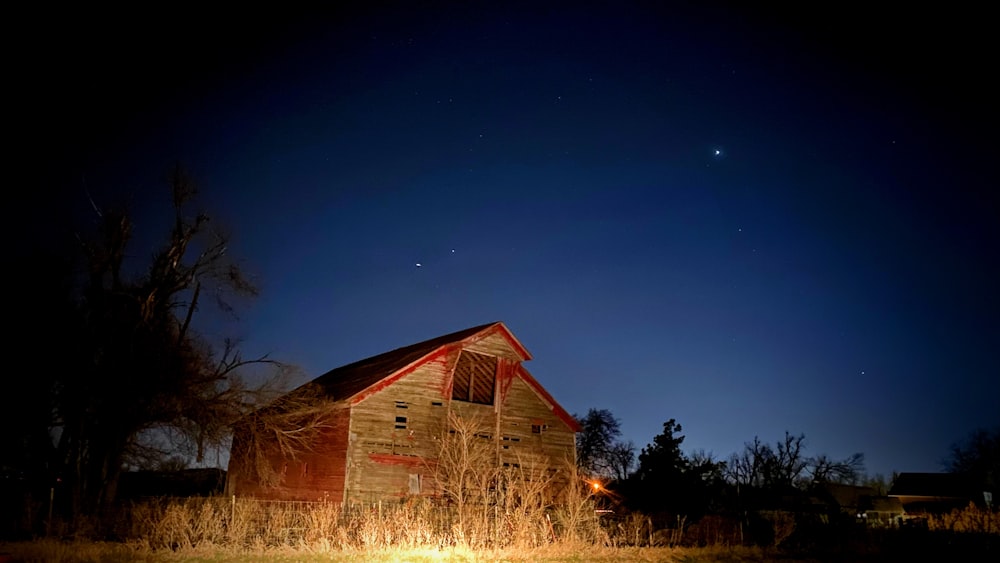 a barn lit up at night with the moon in the sky