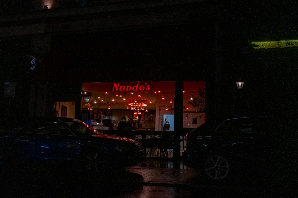 a dark street at night with cars parked in front of a restaurant