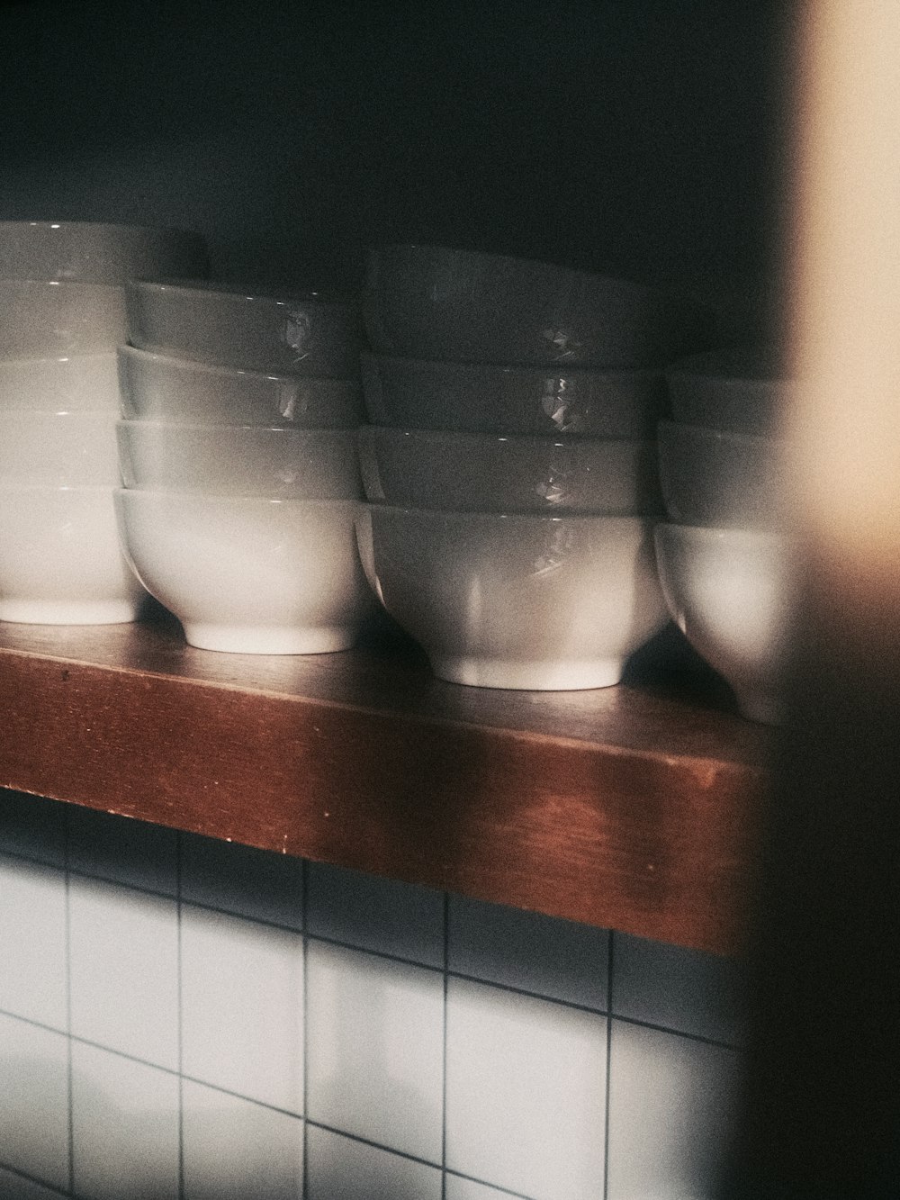 a row of white bowls sitting on top of a wooden shelf