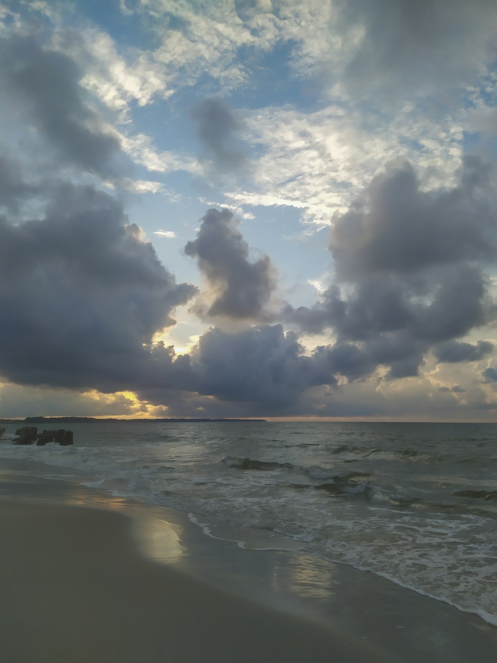 a beach with waves and clouds in the sky