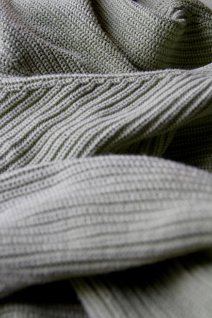 Close-up of hands showing intricate stitching detail on a Lumina Apparel knit sweater.