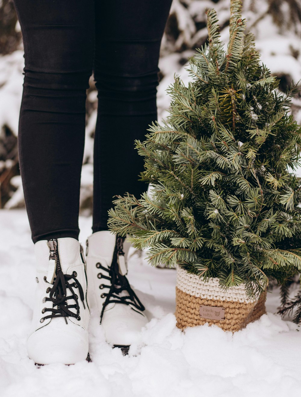 a woman in white boots standing next to a small christmas tree