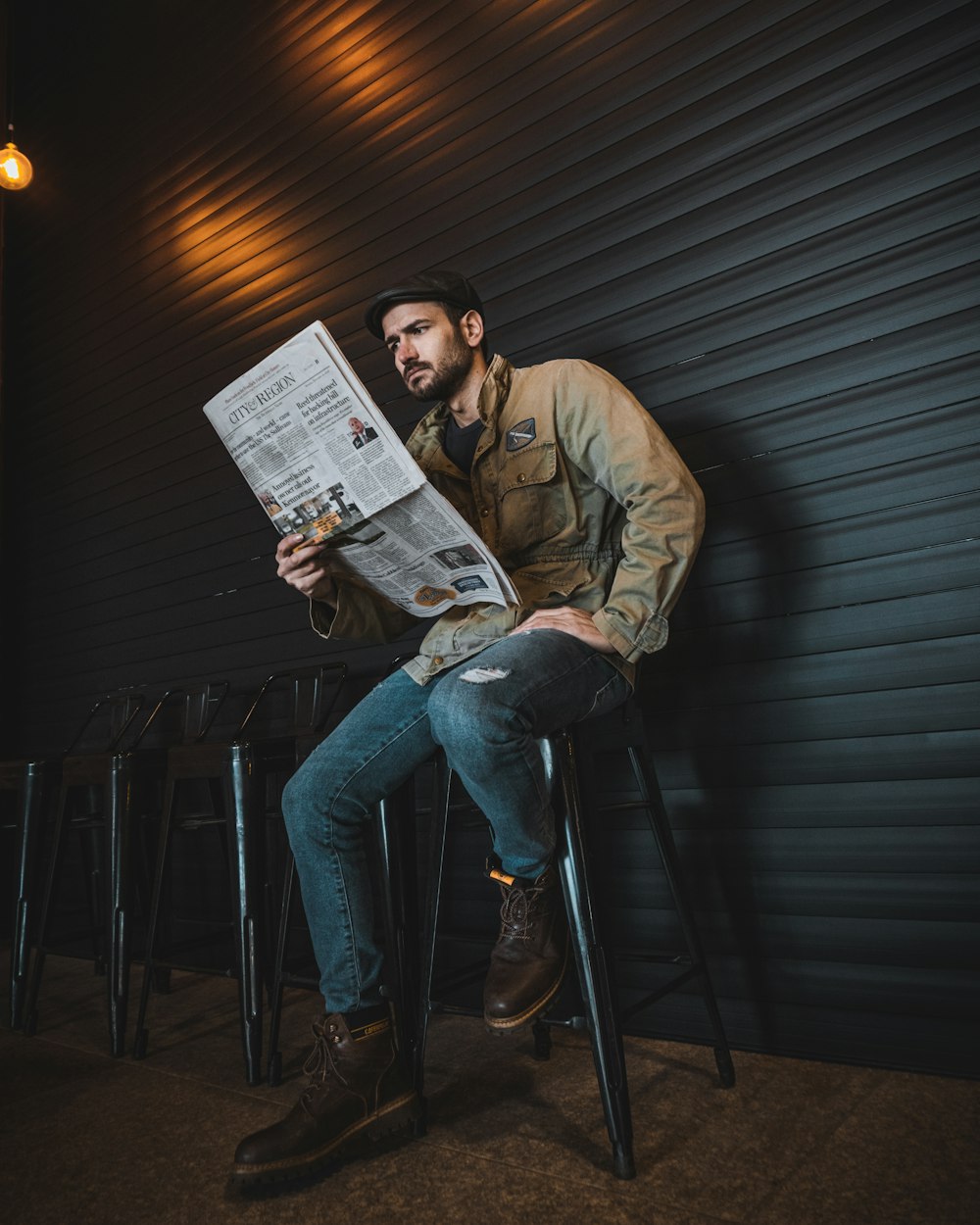 a man sitting on a stool reading a newspaper