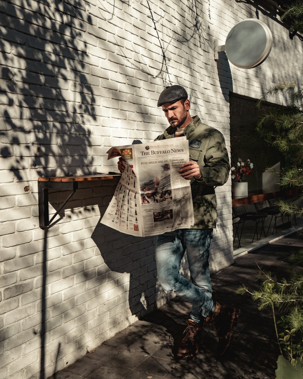 a man standing in front of a brick building while reading a newspaper