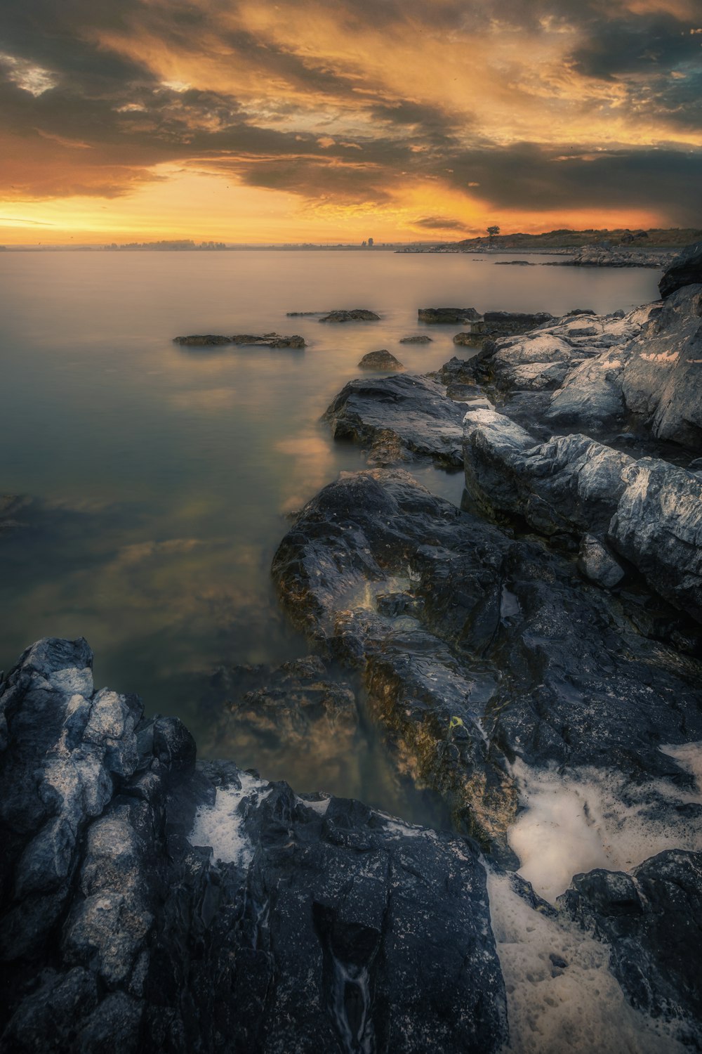 the sun is setting over the water and rocks