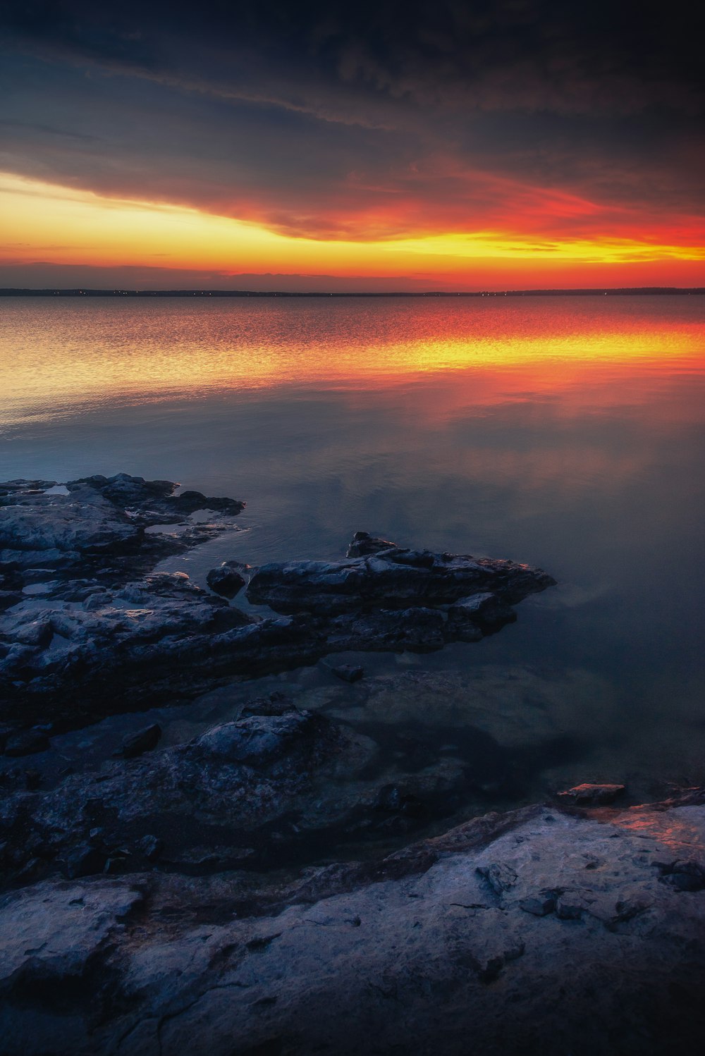 a sunset over a body of water with rocks in the foreground