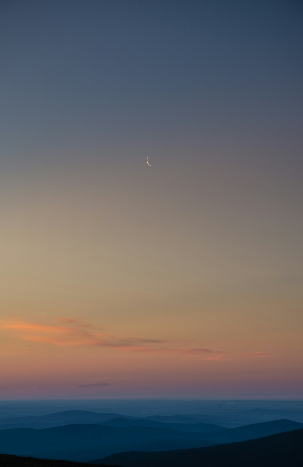 the moon is setting over a mountain range