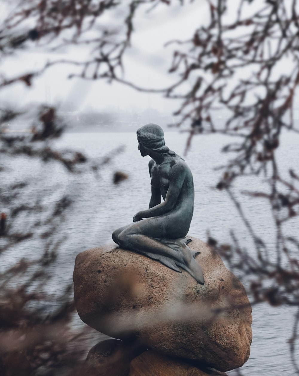 a statue sitting on top of a rock near a body of water