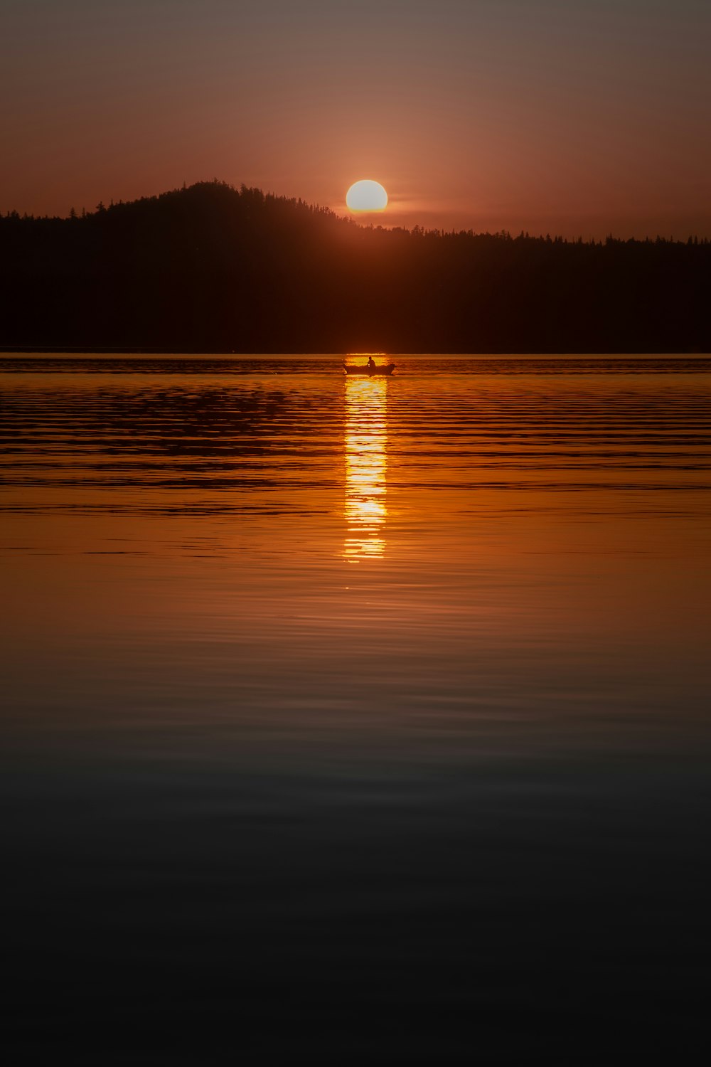 the sun setting over a lake with a boat in the water