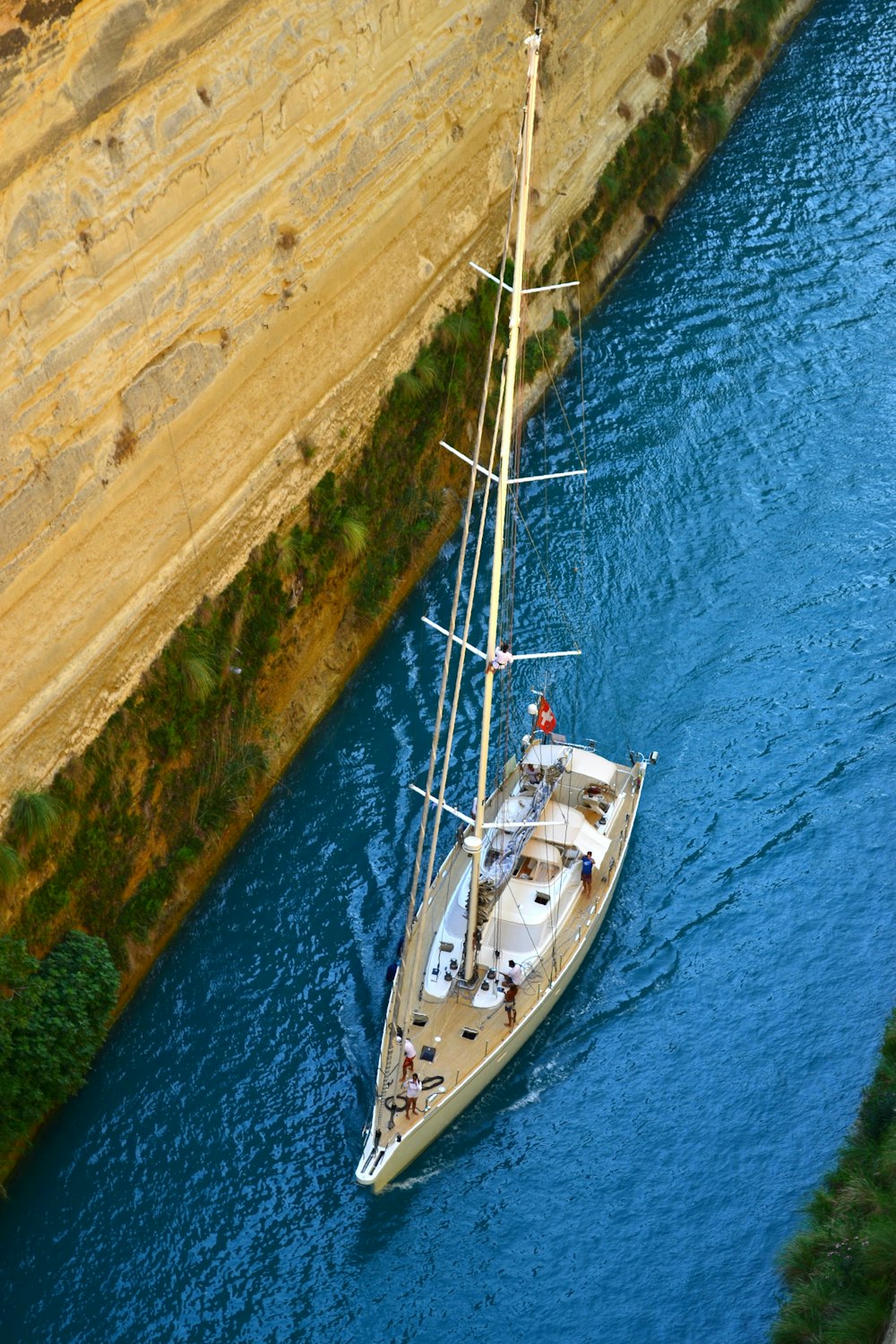 a sailboat sailing down a river next to a cliff