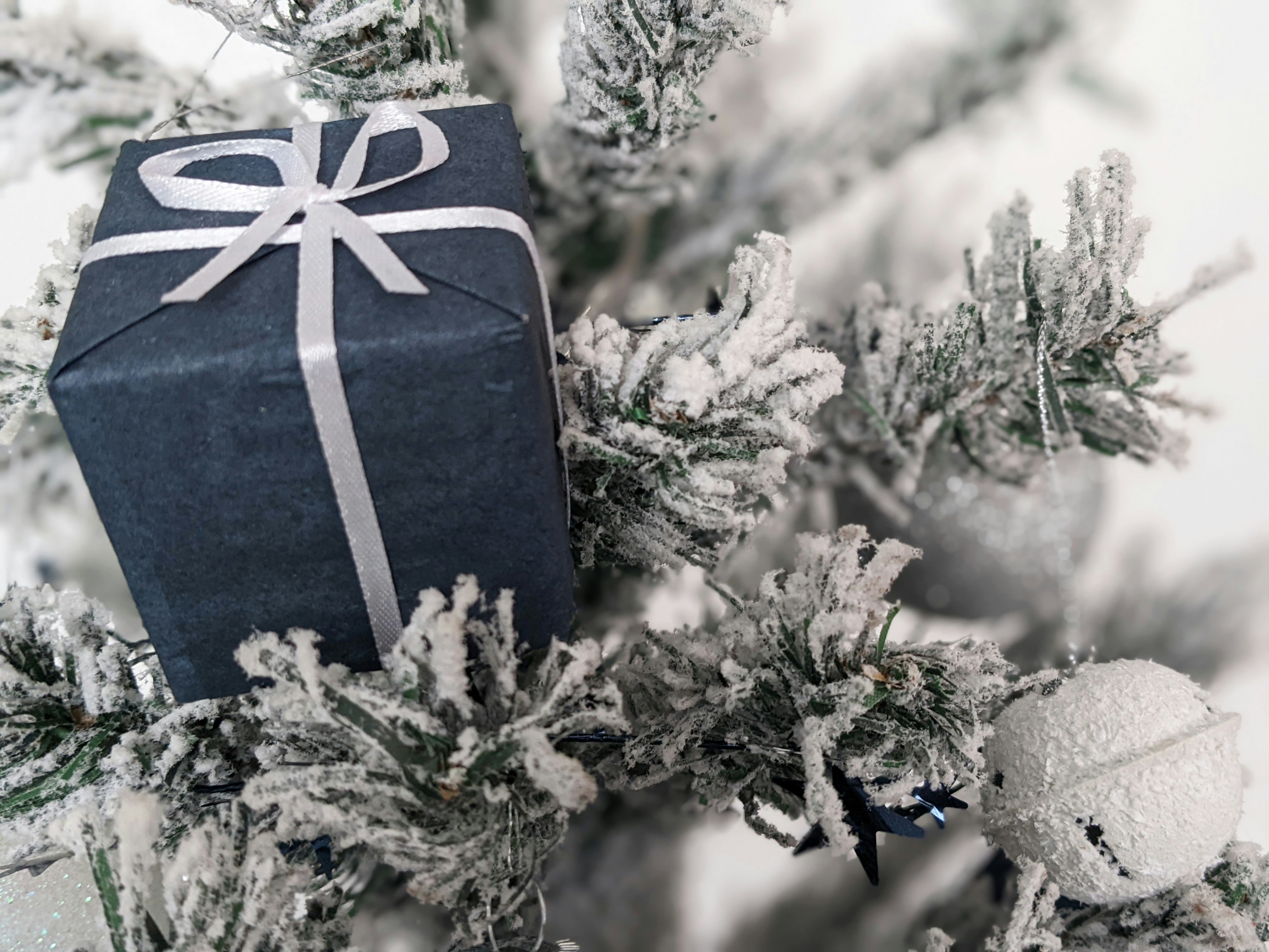 Un regalo envuelto en un papel negro sentado encima de un árbol de Navidad