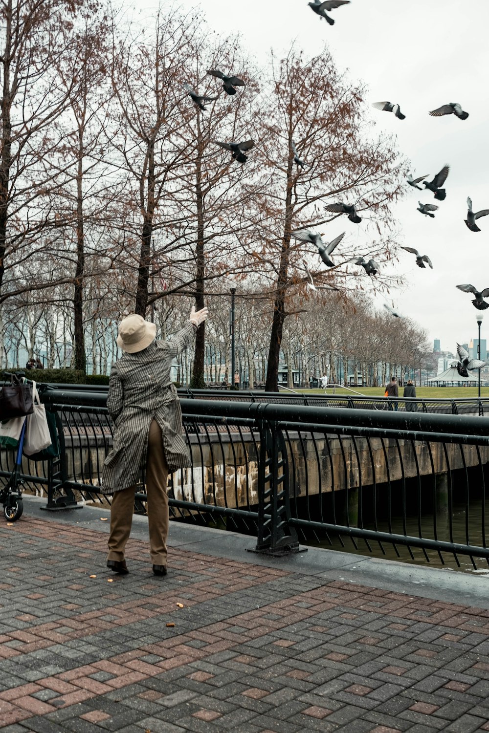 a woman standing on a brick walkway with birds flying overhead