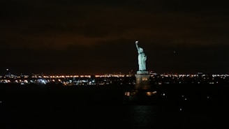 A night skyline of New York City highlighting the Statue of Liberty and skyscrapers.