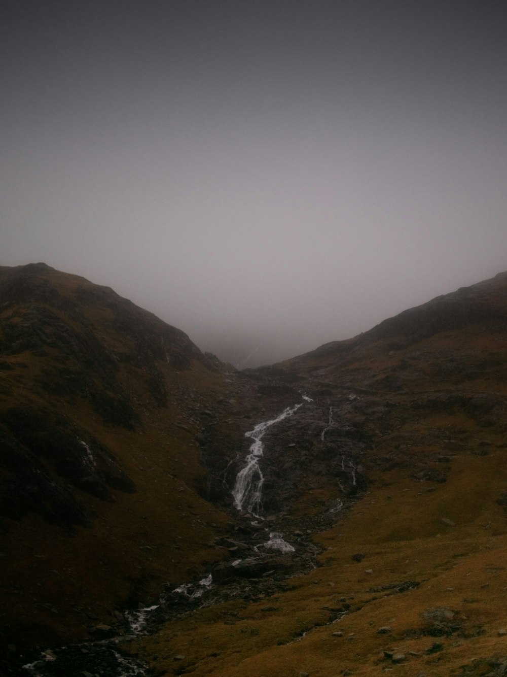 a foggy mountain with a small stream running through it