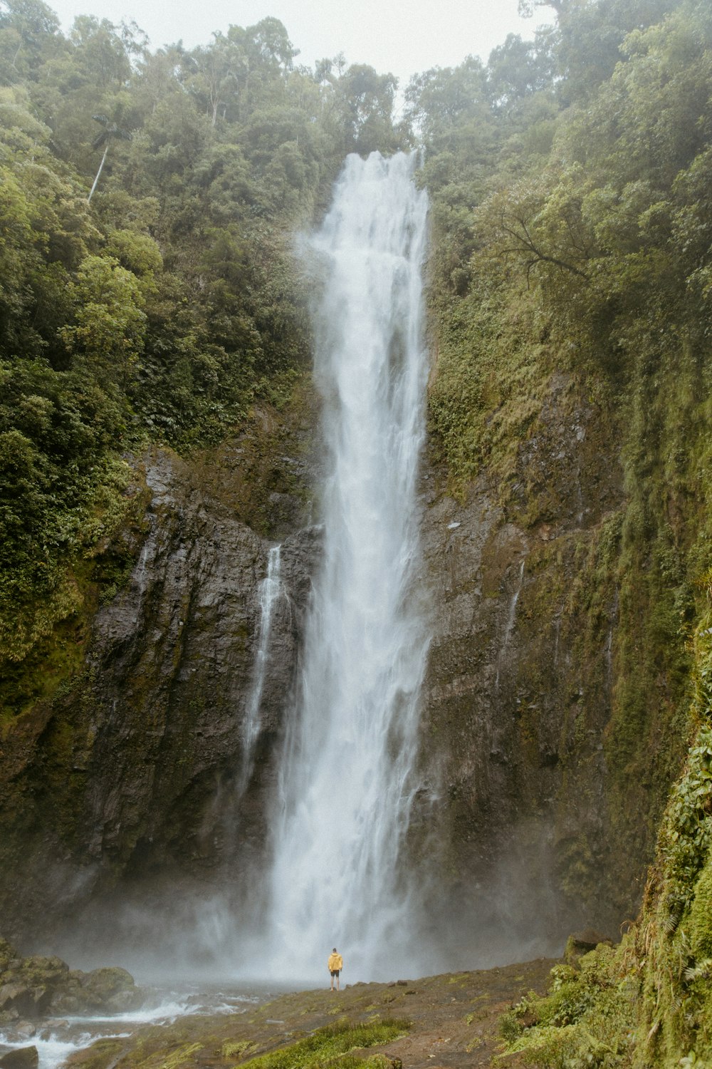 a man standing in front of a tall waterfall