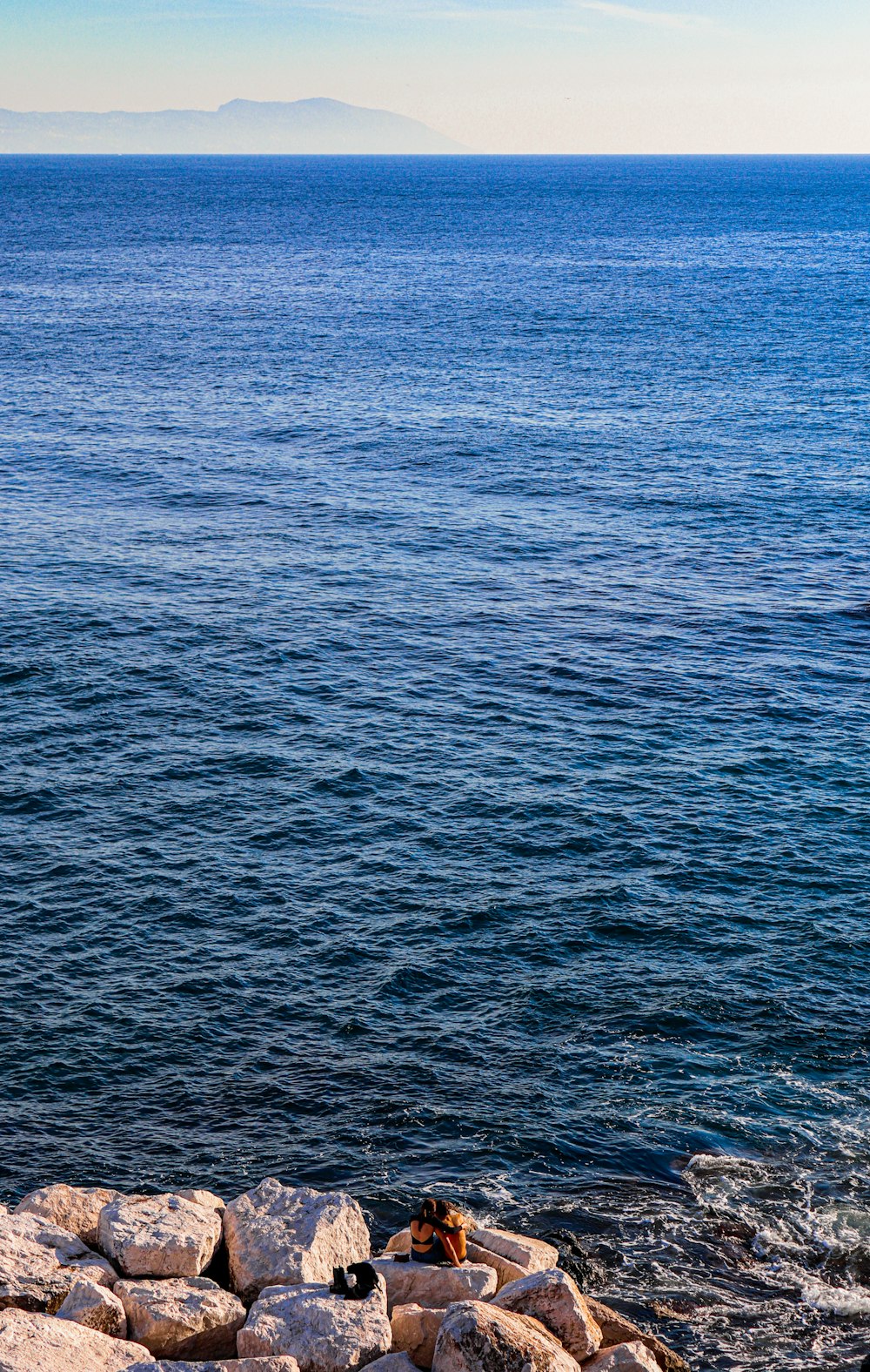 a person sitting on a rock near the ocean