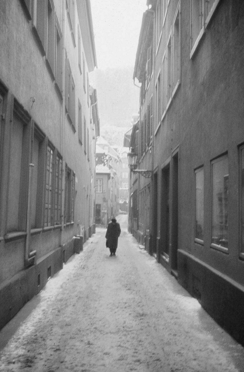 a black and white photo of a person walking down a snowy street