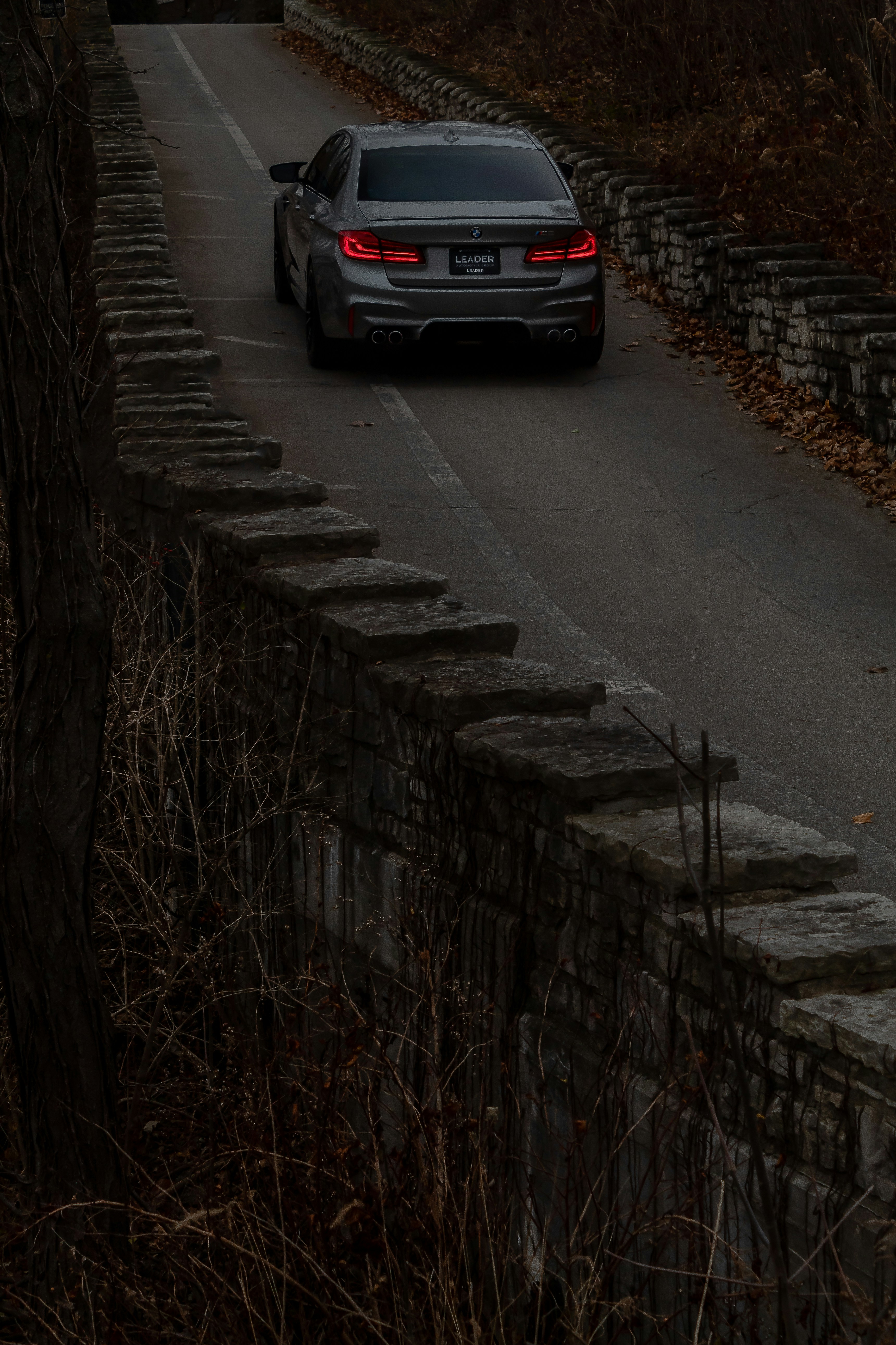 a car driving down a road next to a stone wall
