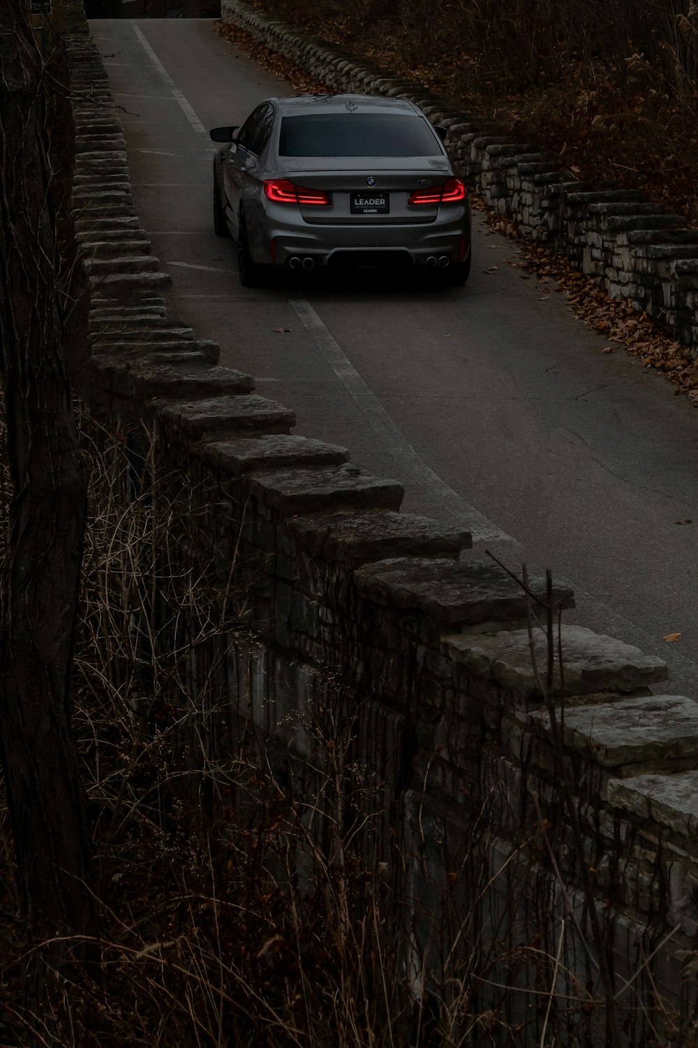 a car driving down a road next to a stone wall