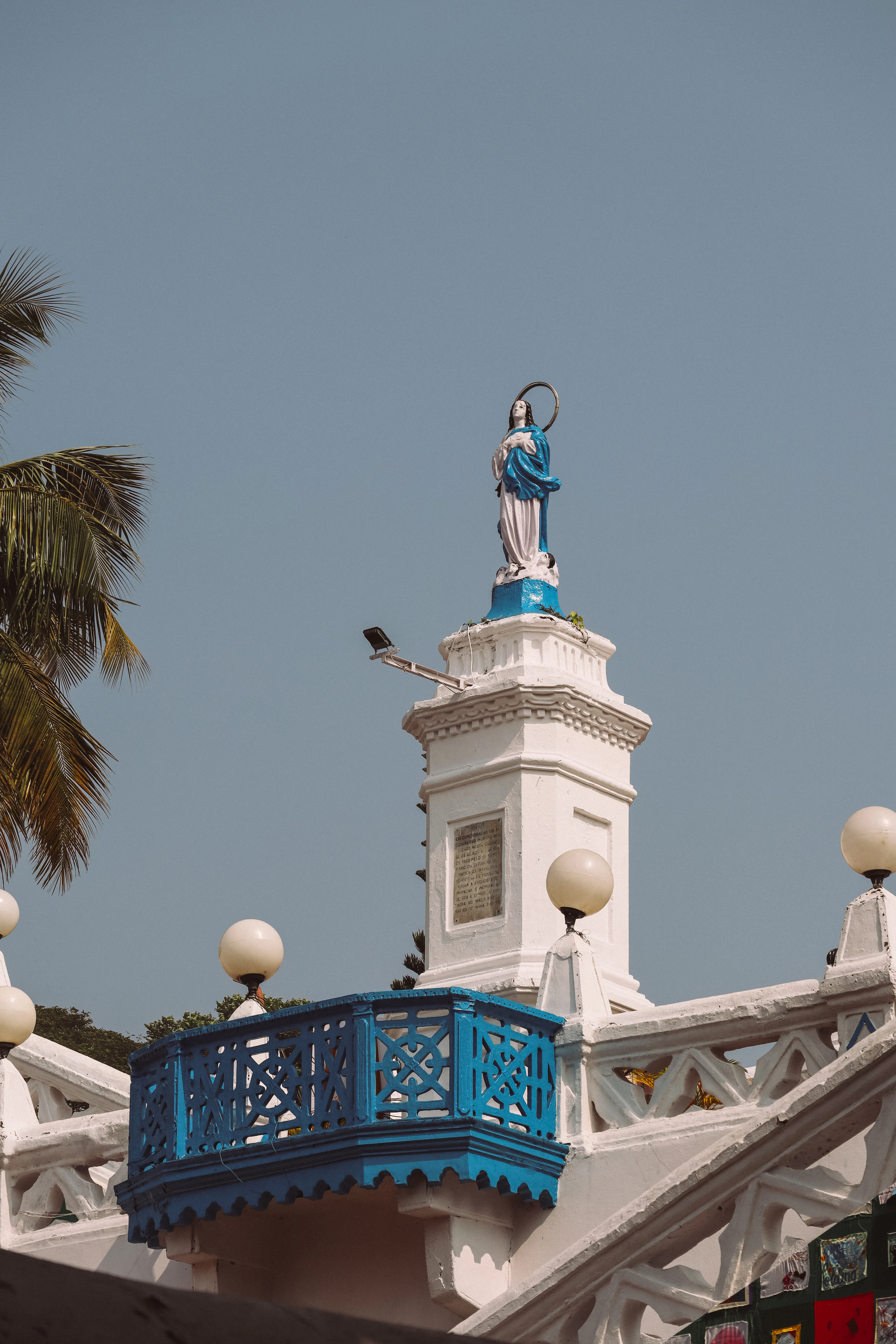 A statue tops a blue lattice balcony on a whitewashed Panaji church against a clear sky.