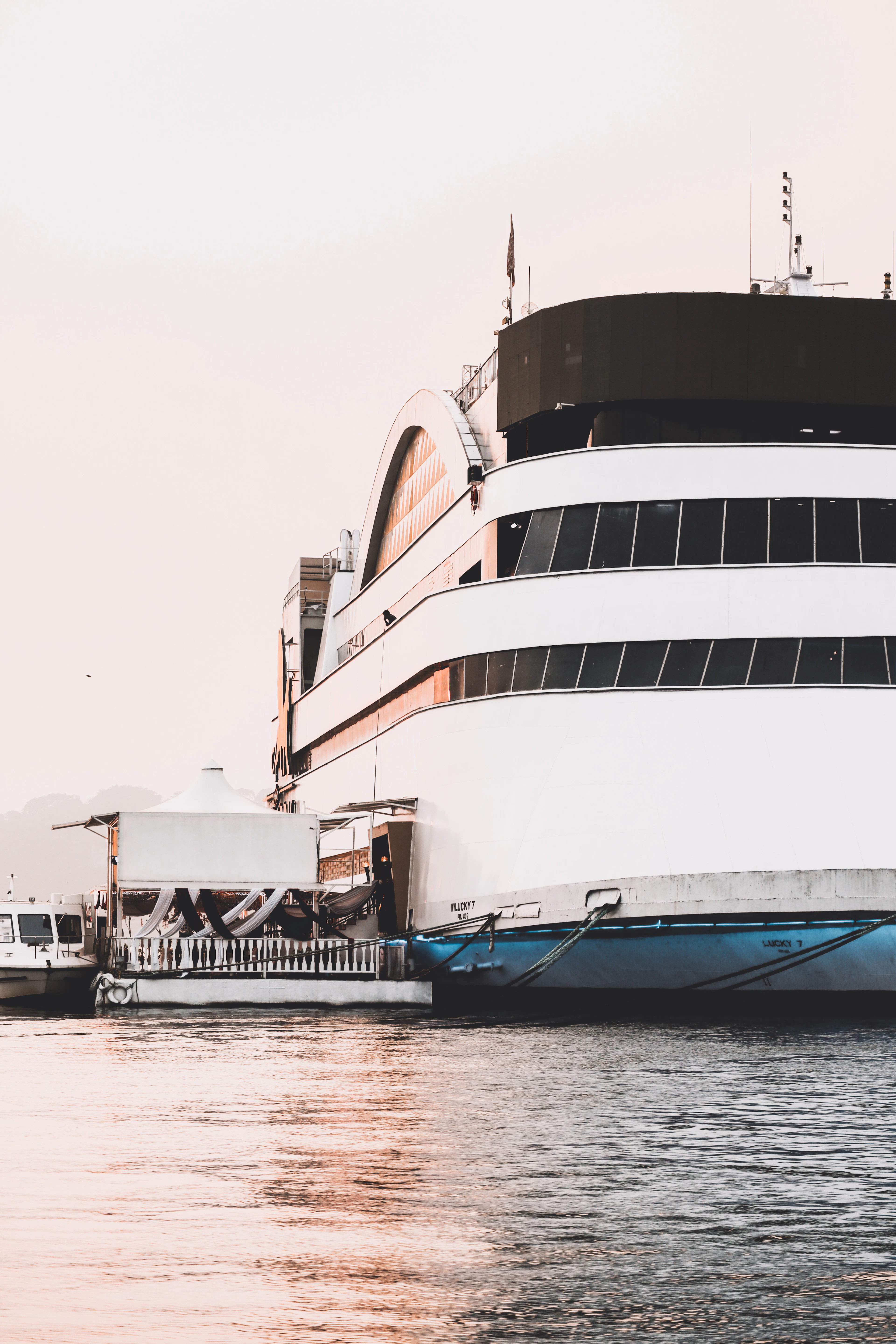 A large white cruise boat with gold ornamental detailing moored on a river at sunset in Goa.