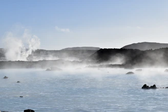 A serene shot of the Furnas volcanic landscape at dawn, with steam rising softly over dark volcanic rocks.