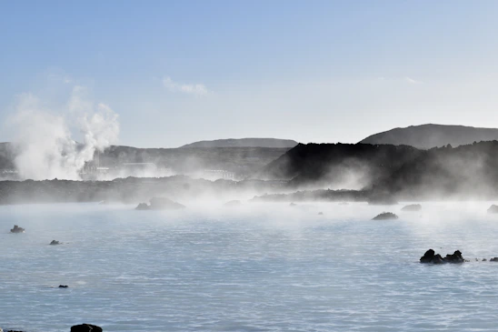 A serene shot of the Furnas volcanic landscape at dawn, with steam rising softly over dark volcanic rocks.