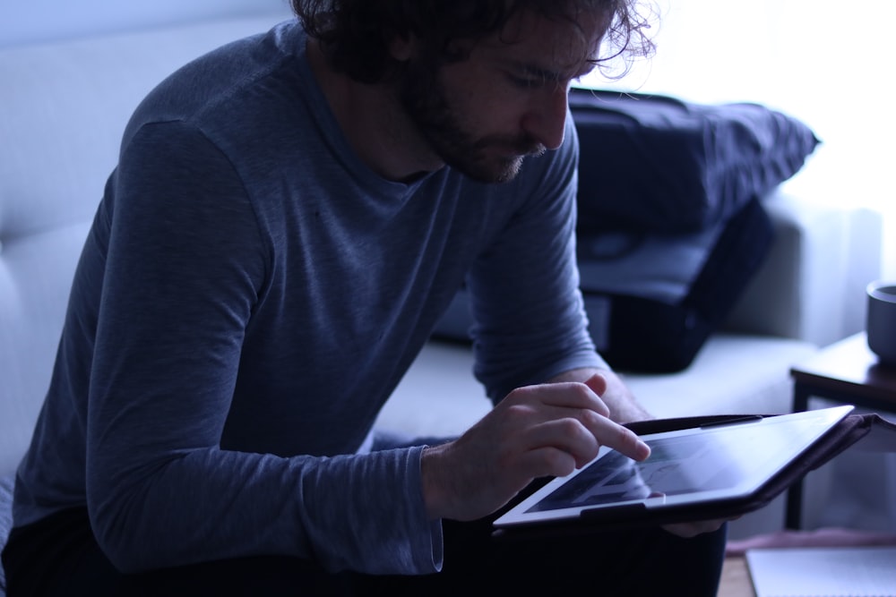 Ein Mann sitzt auf einer Couch und schaut auf ein Tablet