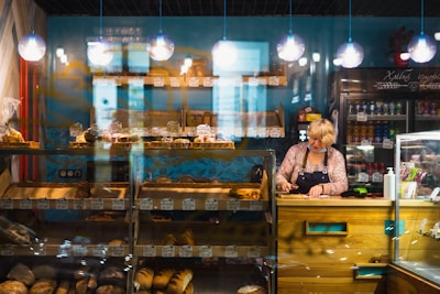 a woman standing behind a counter in a bakery