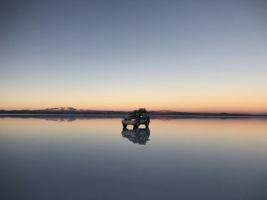 A car is parked on the edge of a large body of water — Salar de Uyuni, Bolivia