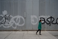 Model wearing a sharp, functional jacket walking briskly past graffiti-covered walls.