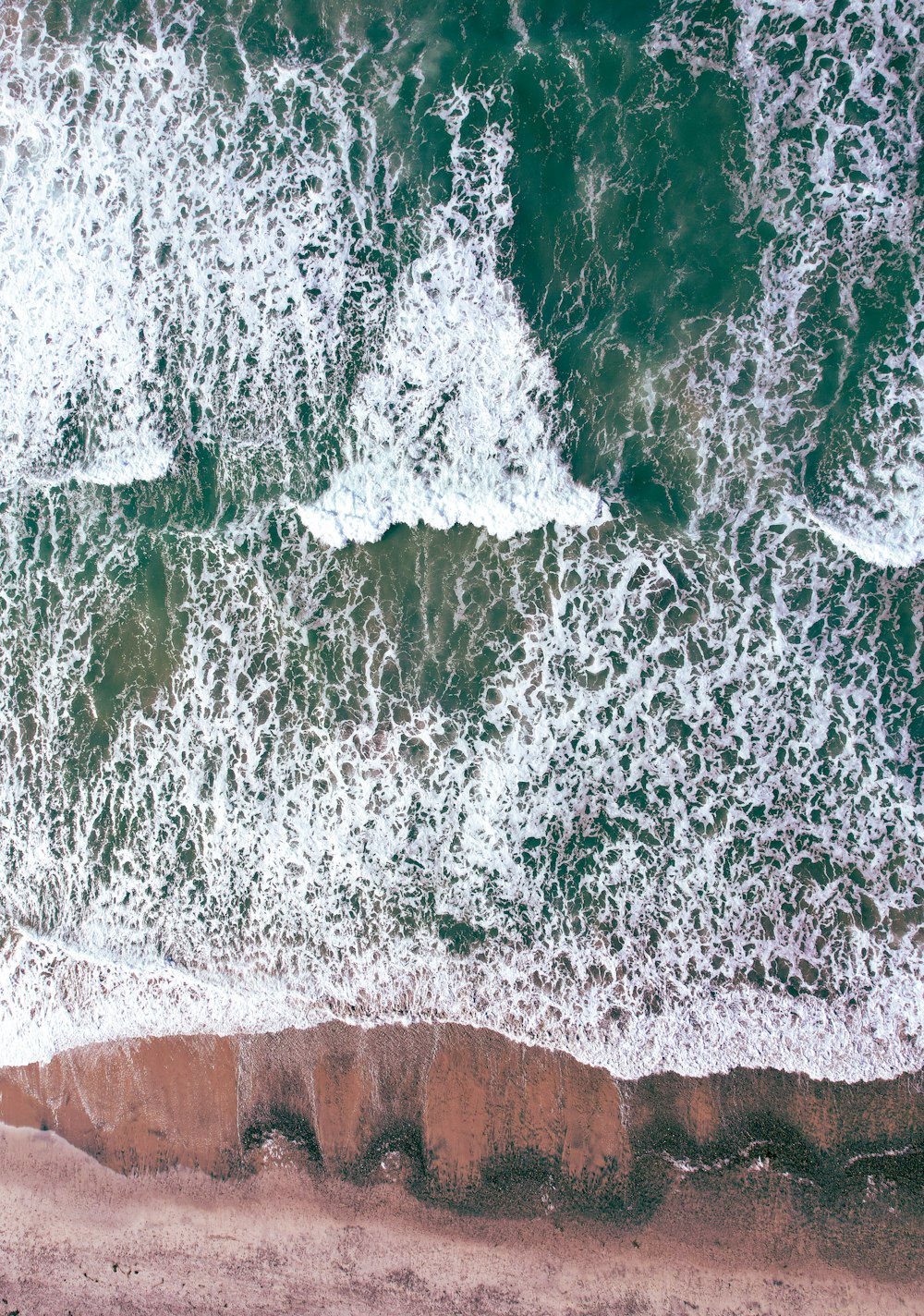 an aerial view of a beach with waves crashing on the shore