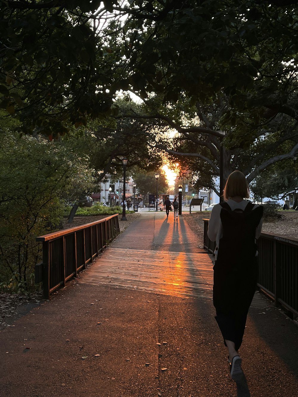 a woman walking down a sidewalk at sunset