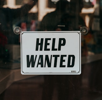 a sign that says help wanted on a glass door