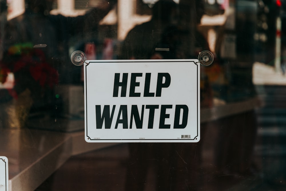 a sign that says help wanted on a glass door